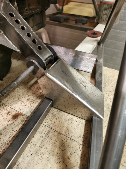 Böjd 2 mm tjock plåtbit monterad i metallkonstruktion på verkstadsbänk.