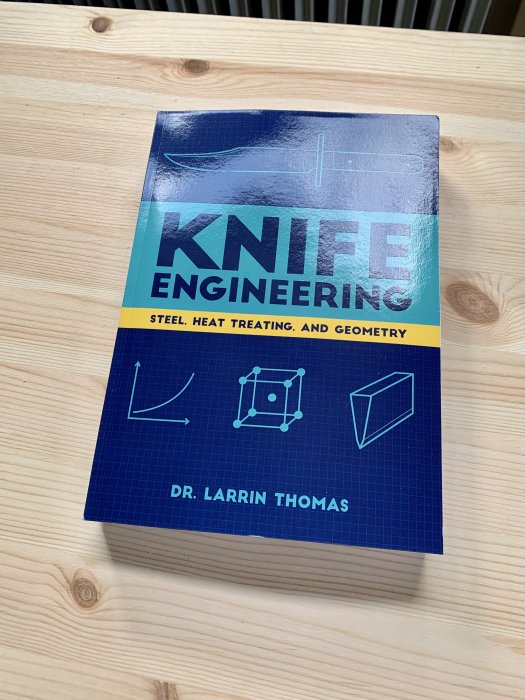 Bok med titeln 'Knife Engineering' av Dr. Larrin Thomas som ligger på ett träbord.