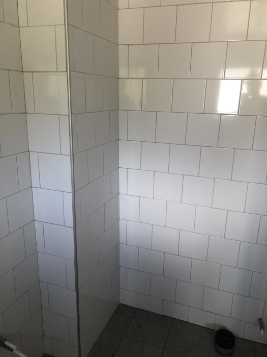 Nylagda vita kakelplattor på vägg och klinkergolv med synlig fogsprång i ett hörn av rummet.