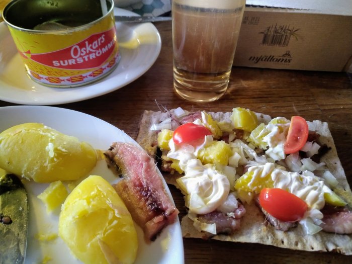 Svensk surströmming på tallrik med tillbehör, bröd, potatis och tomat.