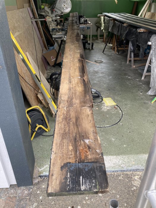 Rutten vindskiva ligger i en verkstad, synliga skador och mögel, omgivna av verktyg och byggmaterial.