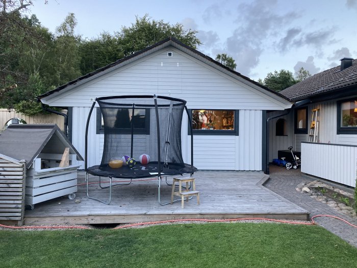 Ett fristående hus med synliga vindskivor och en trädgård med trampolin och barnvagn.