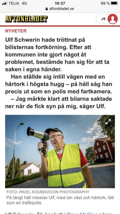Man i reflexväst håller hårtork som en hastighetskamera vid vägkanten.