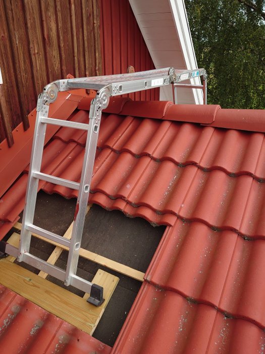 Stege säkert placerad på rött tegeltak med stödplank för tillgång till husvägg som ska målas.