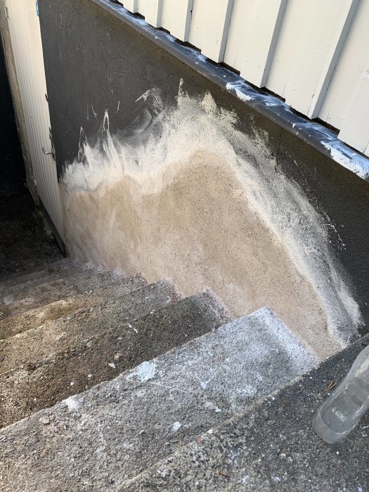 Nyputsad yta på husvägg bredvid trappa med synliga putsarbeten mot mörk grund.