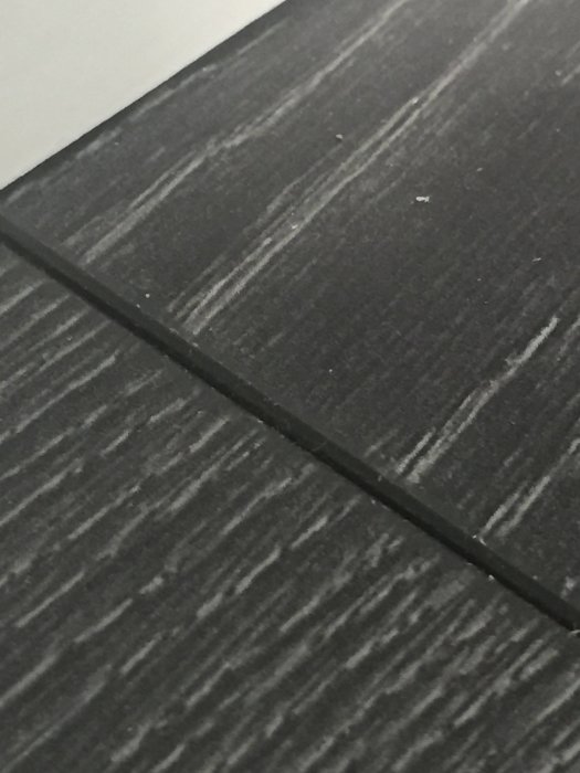Närbild på en mörk laminatgolvplanka med synlig skarv och texturmönster.