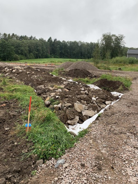 Byggplats med påbörjad grusväg och högar av makadam, stenar, och grävmark.