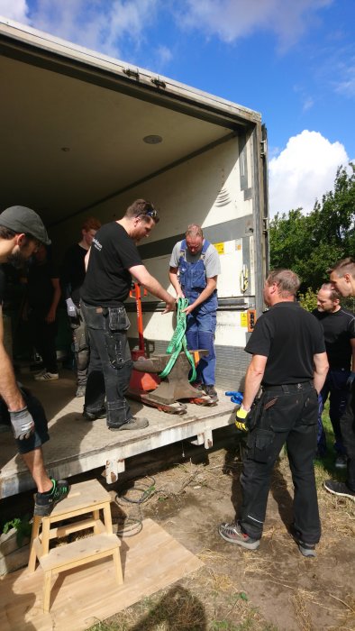 Personer lastar tung utrustning från lastbil med hjälp av pall och spännband.