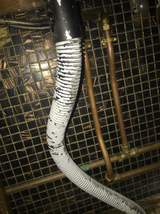 Avloppsrör med flexibel del och anslutna kopparrör under ett handfat, som visar dålig avrinning.