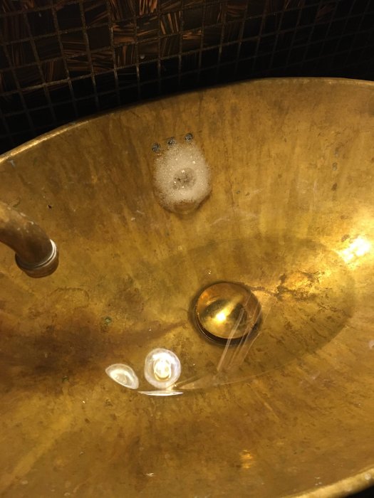 Handfat i gult med vatten och bubblor, pop-up ventil och översvämningsskydd synligt.