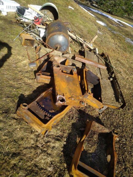 Rostiga gjutjärnssektioner av en panna ihopbultade och demonterade på marken mot en bakgrund med snöfläckar.