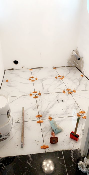 Läggning av marmorliknande kakel med avståndskors och tiling verktyg på ett golv under renovering.