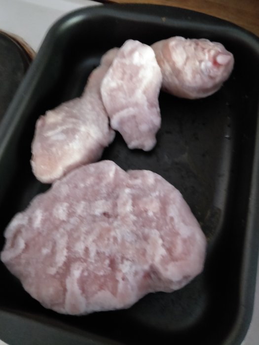 Kycklingfiléer och några ben ligger oförpackade i en svart ugnsform.