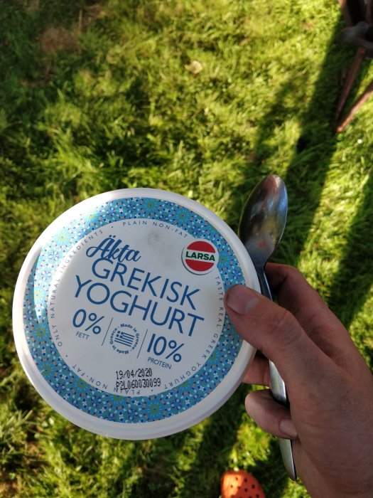 Hand håller ett yoghurtlock och sked; spelar på borax, inte yoghurt, i renoveringsprojekt.