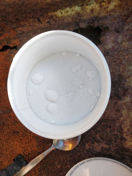 Vitt pulver, borax, i en plastkopp på en rostig yta, inte yougurt.