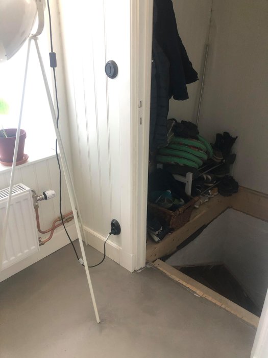 En öppen källartrappa med en synlig luftspalt vid kanten där syllen möter golvet, intill en ytterdörr och skor.