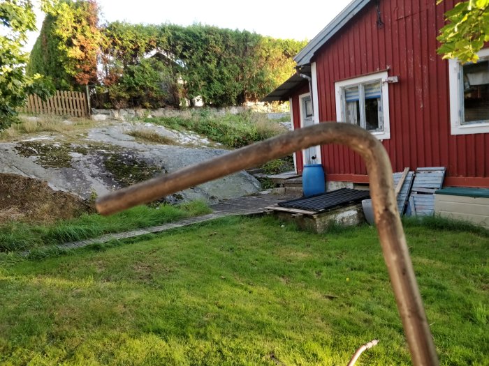 Bild på en hemgjord bänktving med ojämn värmebehandling framför en röd stuga och gräsmatta.