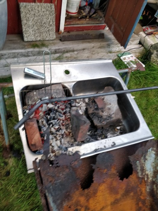 Gammal rostig grill konstruerad av en återanvänd köksvask fylld med grillkol och tegel.