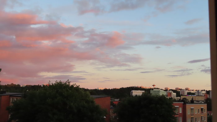 Solnedgång över stadslandskap med färgglad himmel och siluetter av byggnader och träd.