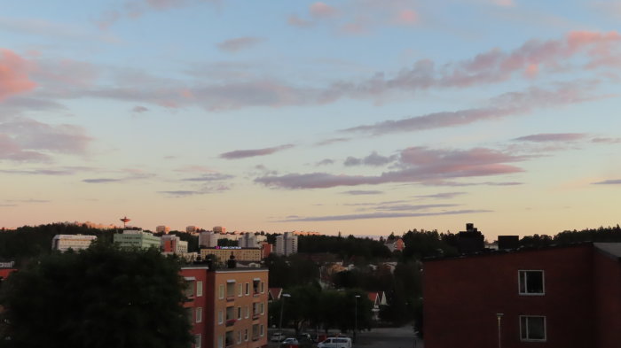 Solnedgång över en stad med silhuetter av byggnader och pastellfärgad himmel.