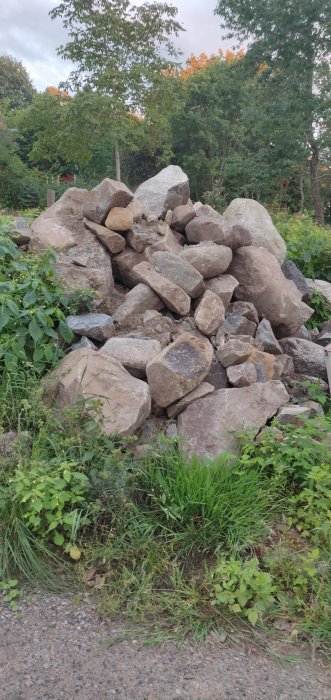 En hög med oregelbundna stenar i olika storlekar vid sidan av en väg, med grönska i bakgrunden.