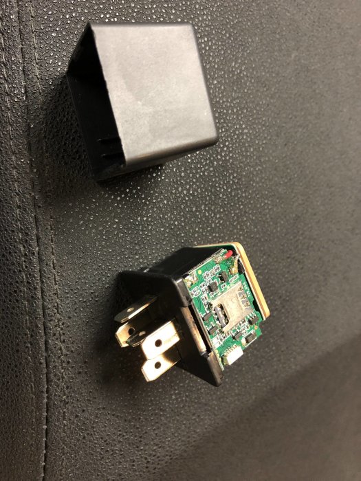 En öppen elektronisk spårningsenhet från AliExpress vid sidan av dess svarta plasthölje.