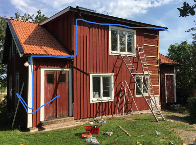 Röd trähusfasad med hängrännor och stuprör, verktyg på marken. Markeringar visar vattenflöde från tak.