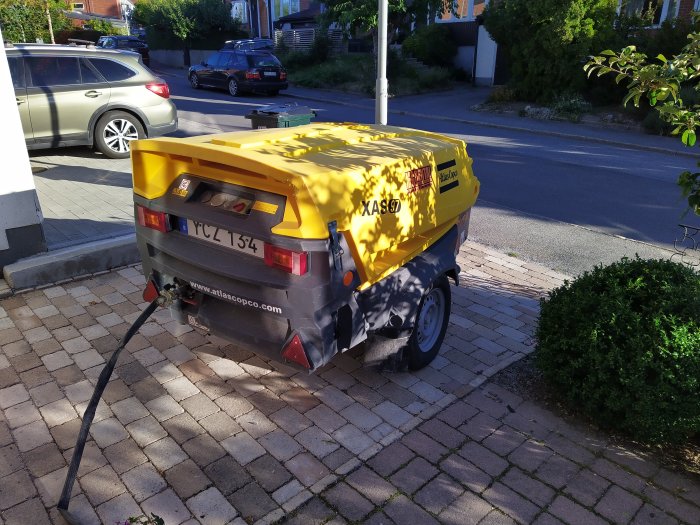 Gul Atlas Copco kompressor på en inhägnad uteplats i soligt morgonljus.