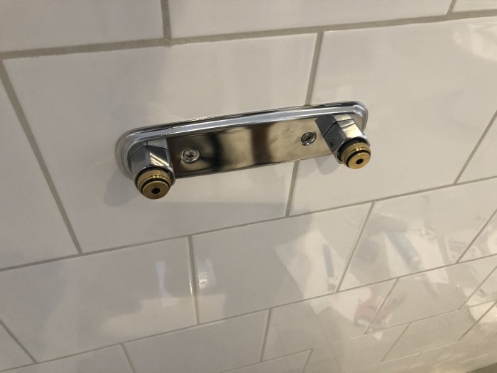 Kromad badrumsfördelare monterad på kaklad vägg, redo för anslutning av badrumsarmatur.