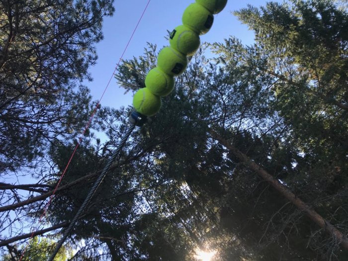 Hemmagjord dämpning med tennisbollar trädda på vajer bland träd, med rörisolering och dörrstopp synligt.