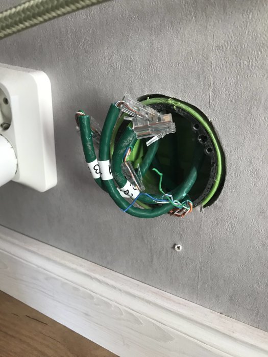 Öppen eldosa i vägg med Ethernet-kablar och plastklämmor, redo för elektrikerinspektion.