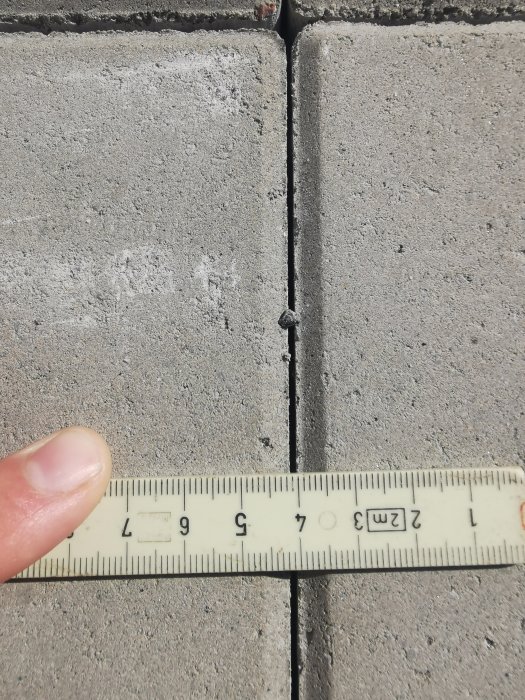 Närbild på mätning av fogbredd mellan betongplattor med tumstock som visar cirka 1 mm.