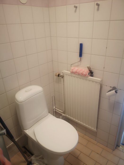 Före-bild av badrum före renovering, visar vit toalett, beige kakel och traditionell radiator.