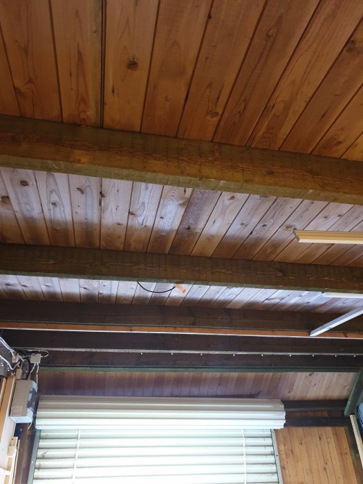 Inredning av ett kallgarage med träpanel i taket, exponerade takbjälkar och en öppen garageport.