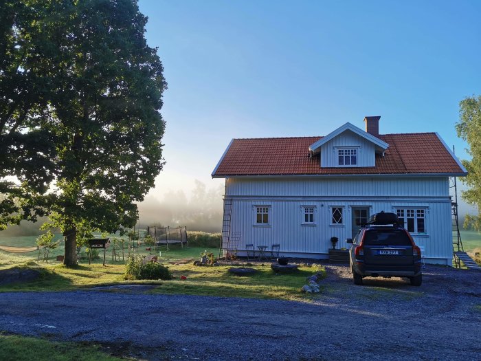 Morgonvy av ett tvåvåningshus med nylagt panel på gaveln och en bil framför, med dimma i bakgrunden.