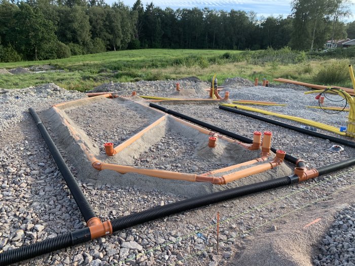 Nylagda avloppsrör och makadam i ett pågående byggprojekt för husgrund.