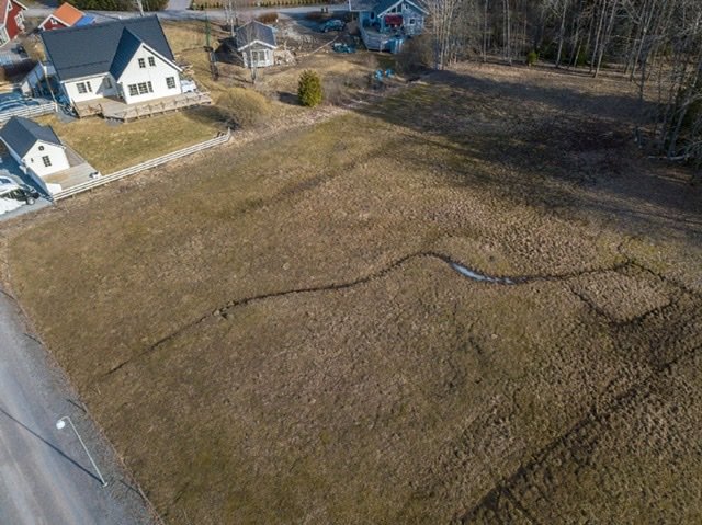 Flygfoto över tomtmark med enstaka hus och träd i omgivningen.