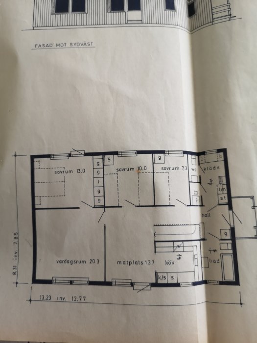 Ritning av husets planlösning med markerade sovrum, vardagsrum, kök och andra utrymmen.