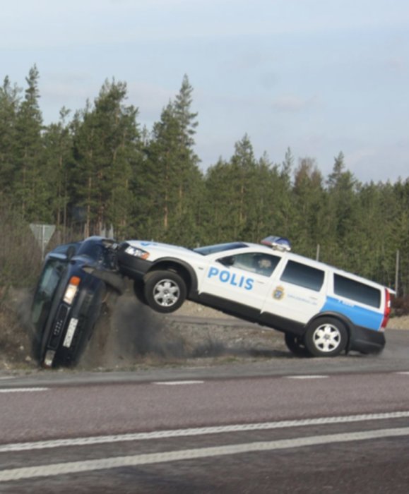 Polisbil som utför en prejning på en annan bil vid sidan av en väg omgiven av skog.