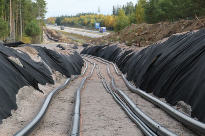 Ledningar i en grävd fåra vid sidan av en väg, täckt med svart fiberduk, som en del av Sydvästlänkens byggprojekt.