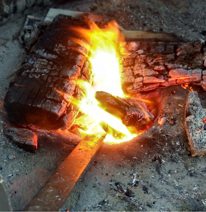 Glowing fire with a metal rod in a homemade forge, no visible smoke, demonstrating renovation process.