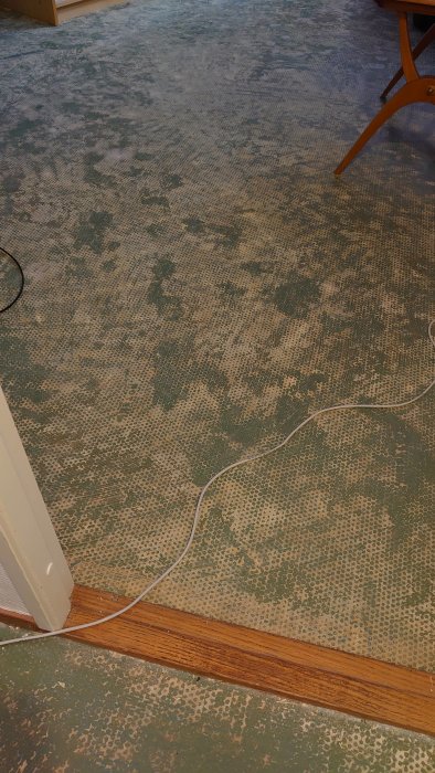 Källargolv där en heltäckningsmatta tagits bort, visar gröna rester av färg och vita gummirester.