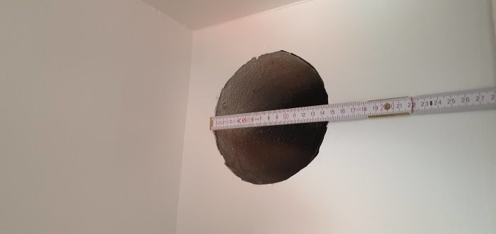 Ventilationshål i väggen mätt med måttband som visar 145 mm i diameter.