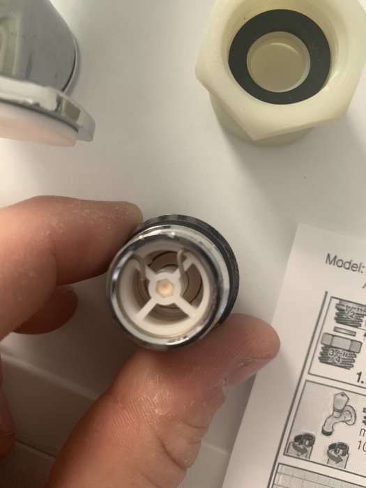 Hand håller en del av rörkoppling eller ventil med plast och metallkomponenter.