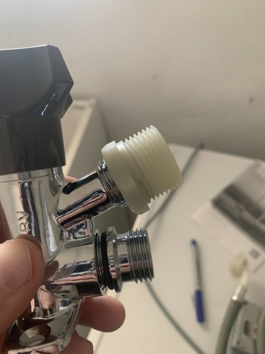 Hand håller en kromad blandare med en vit plastadapter.