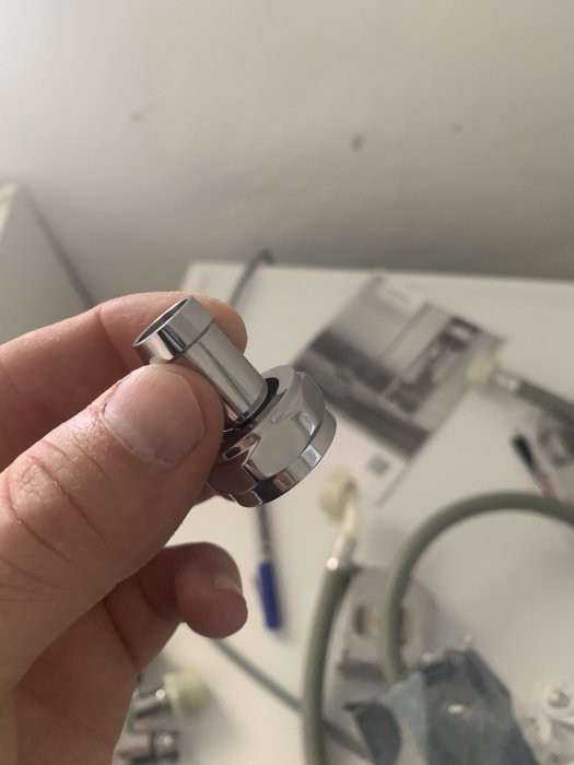 Hand håller en metall ventil eller anslutning med oskarp bakgrund av byggarbetsplats.