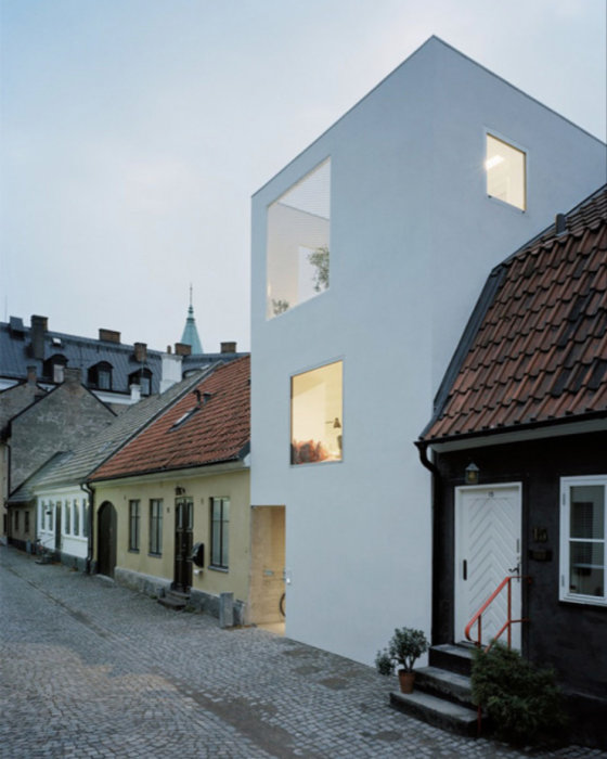 Modern vit arkitektur vid en kullerstensgata bland traditionella hus, Stadsbyggnadspris-vinnare i Landskrona.