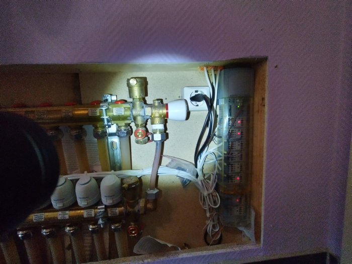 Öppen termostatcentral med golvvärmeslingor, ventiler och ett vred märkt med "m H2O" i en husinstallation.