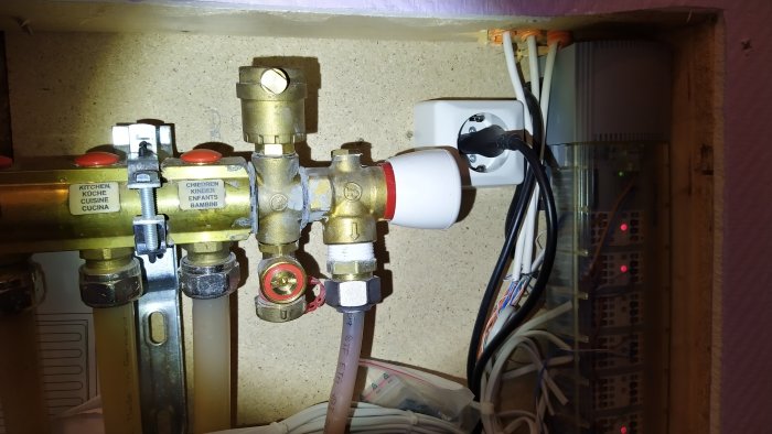 Inredning med golvvärmefördelare och termostater, mätare med rött vred och skala märkt "m H2O".