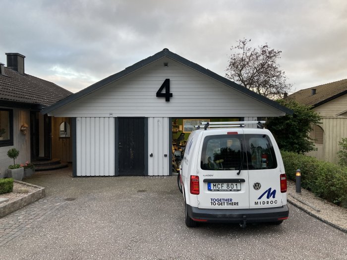 Vitmålad fristående garagebyggnad med nya vindskivor och företagsbil parkerad framför.